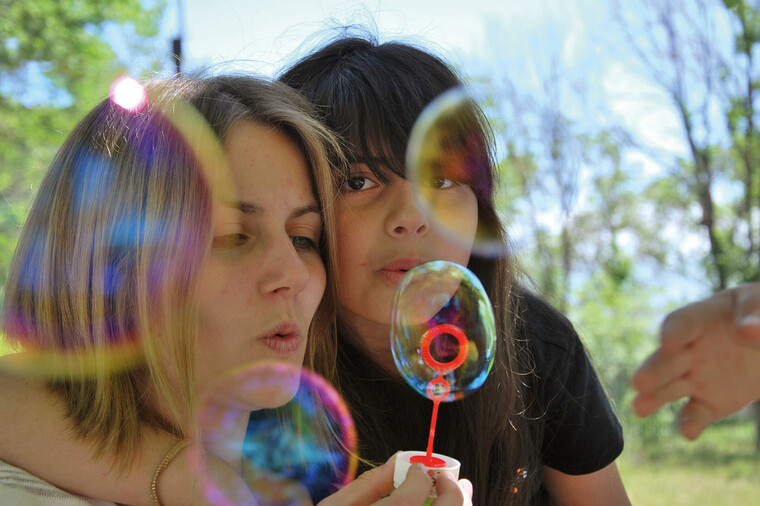 Eine junge Frau und ein Kind machen Seifenblasen in der Natur.
